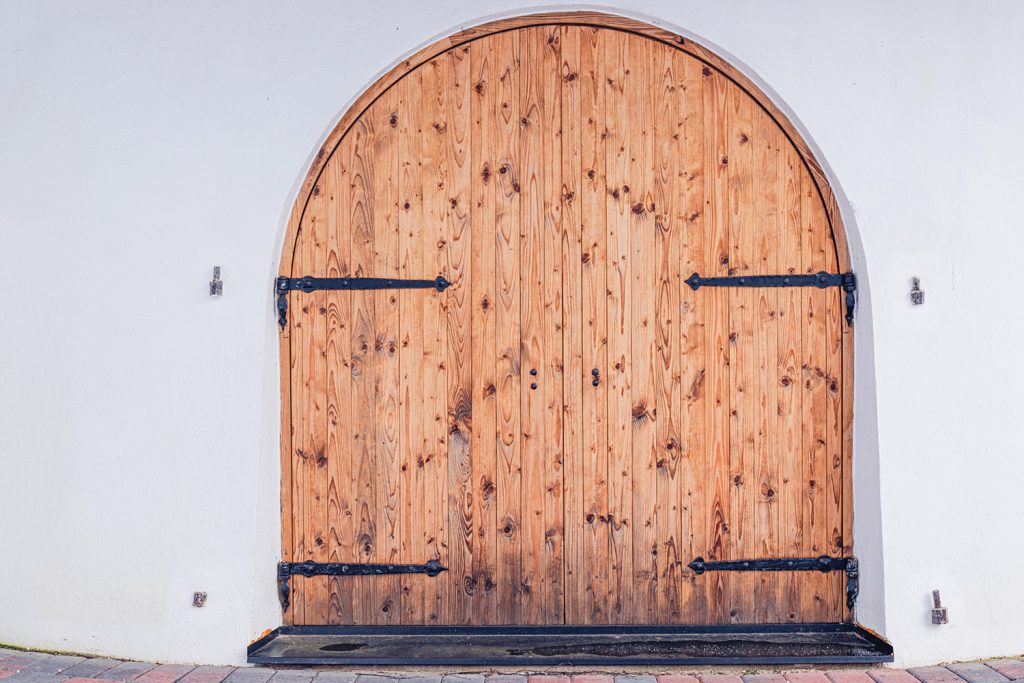 porte extérieure en bois arrondie avec des planchettes verticales et garnitures en fer forgé