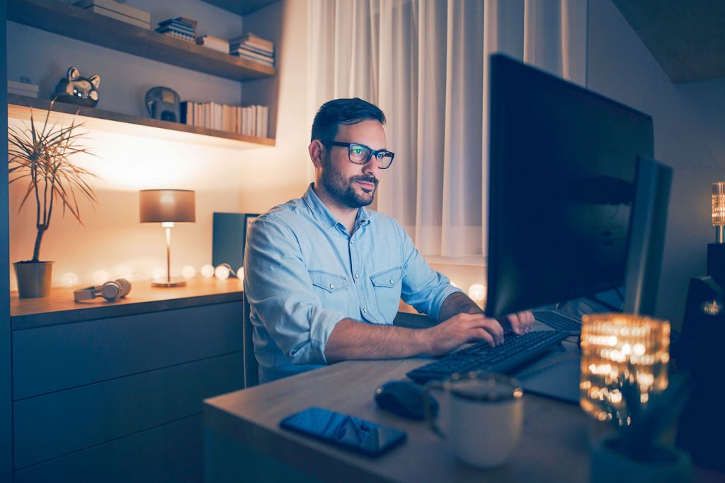 un homme travaille le soir à domicile devant son PC avec une lumière d’ambiance