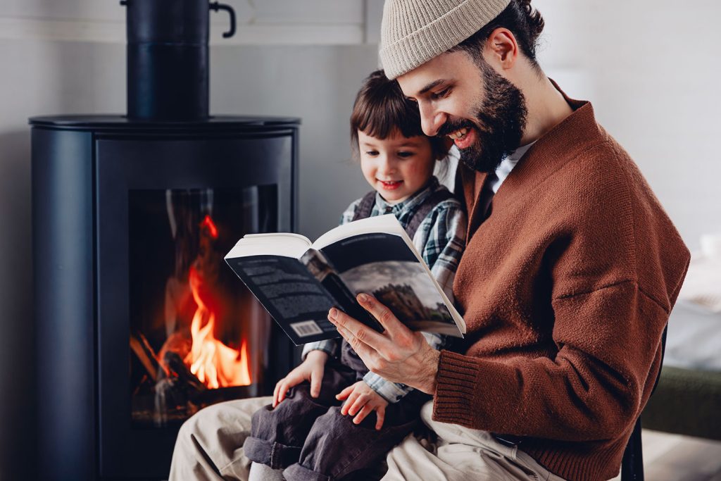 père lit un livre à sa fille près d’un poêle aux pellets