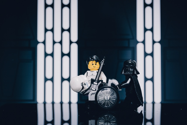Decor van lego met Darth Vader die een rolstoel voortduwt voor een stormtrooper die zijn helm heeft afgezet 
