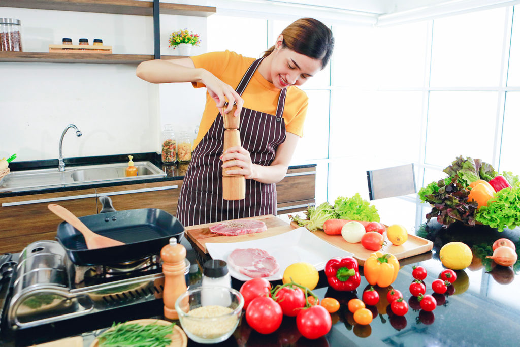 vrouw kruidt vlees met pepermolen aan groot keukeneiland