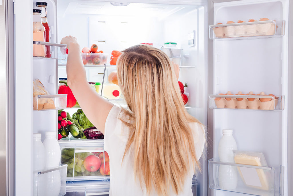jonge vrouw zoekt eten in koelkast