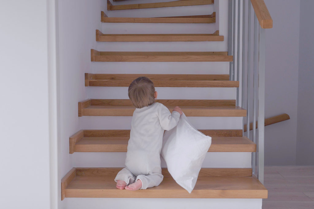 un jeune enfant monte un escalier en bois avec un oreiller