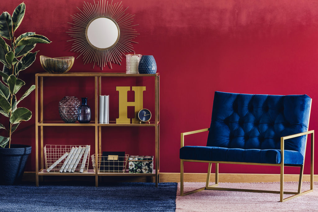 blauwe zetel en gouden boekenrekje tegen rode woonkamermuur