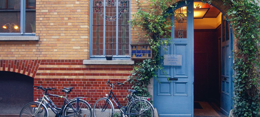 Alt tekst : vélo devant la façade d’une maison de ville avec une porte bleue