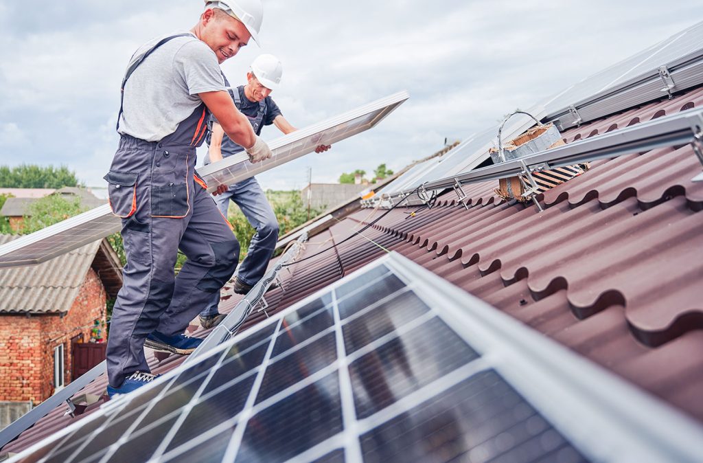 deux hommes placent des panneaux photovoltaïques sur un toit