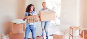 deux femmes portant des cartons de déménagement entrent dans une maison