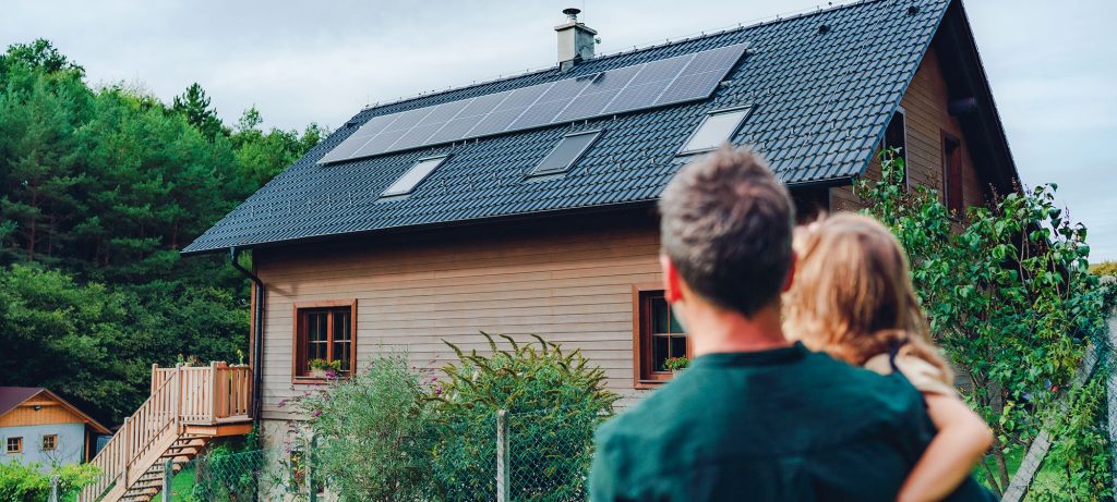 homme et enfants regardent une maison en bois avec panneaux photovoltaïques