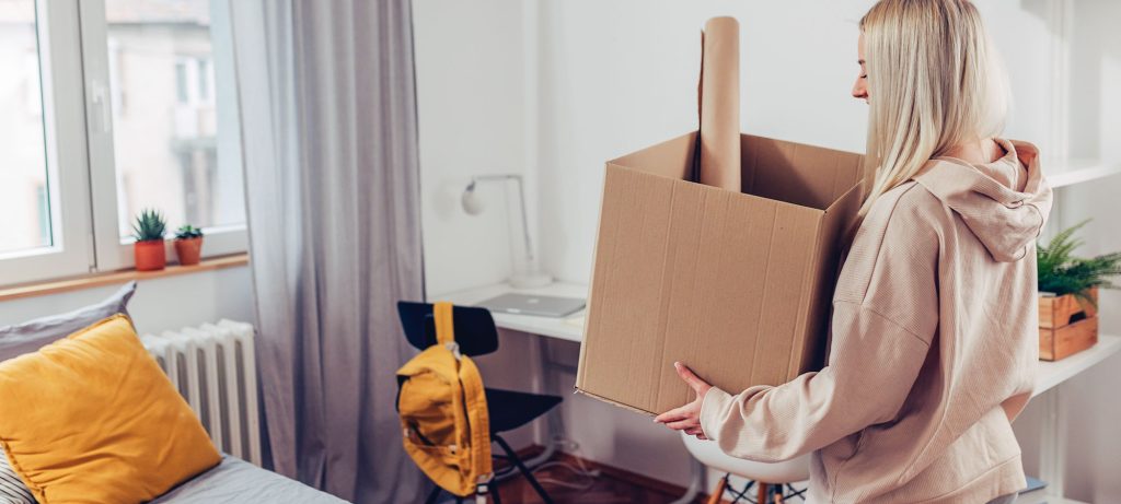 jeune femme avec caisse de déménagement dans kot d’étudiant