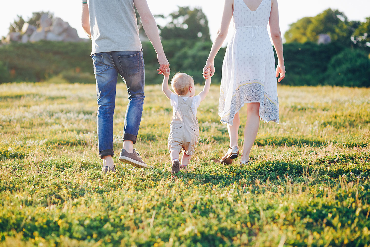 bambin court dans l’herbe main dans la main avec son papa et sa maman